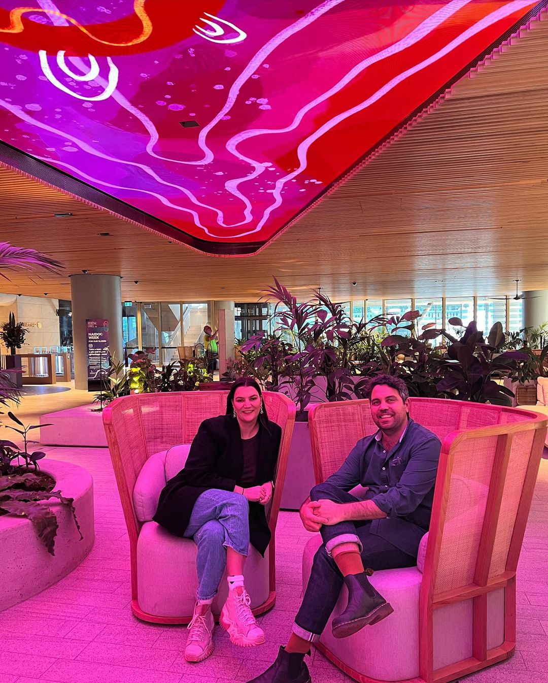 Two people sitting on contemporary under a digital art screen in a commercial lobby