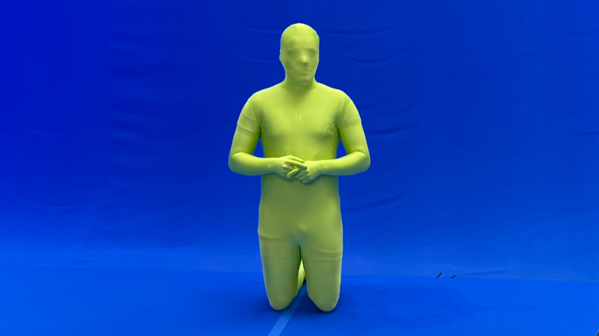 Person wearing green screen suit standing on his knees on blue screen visual effects studio.