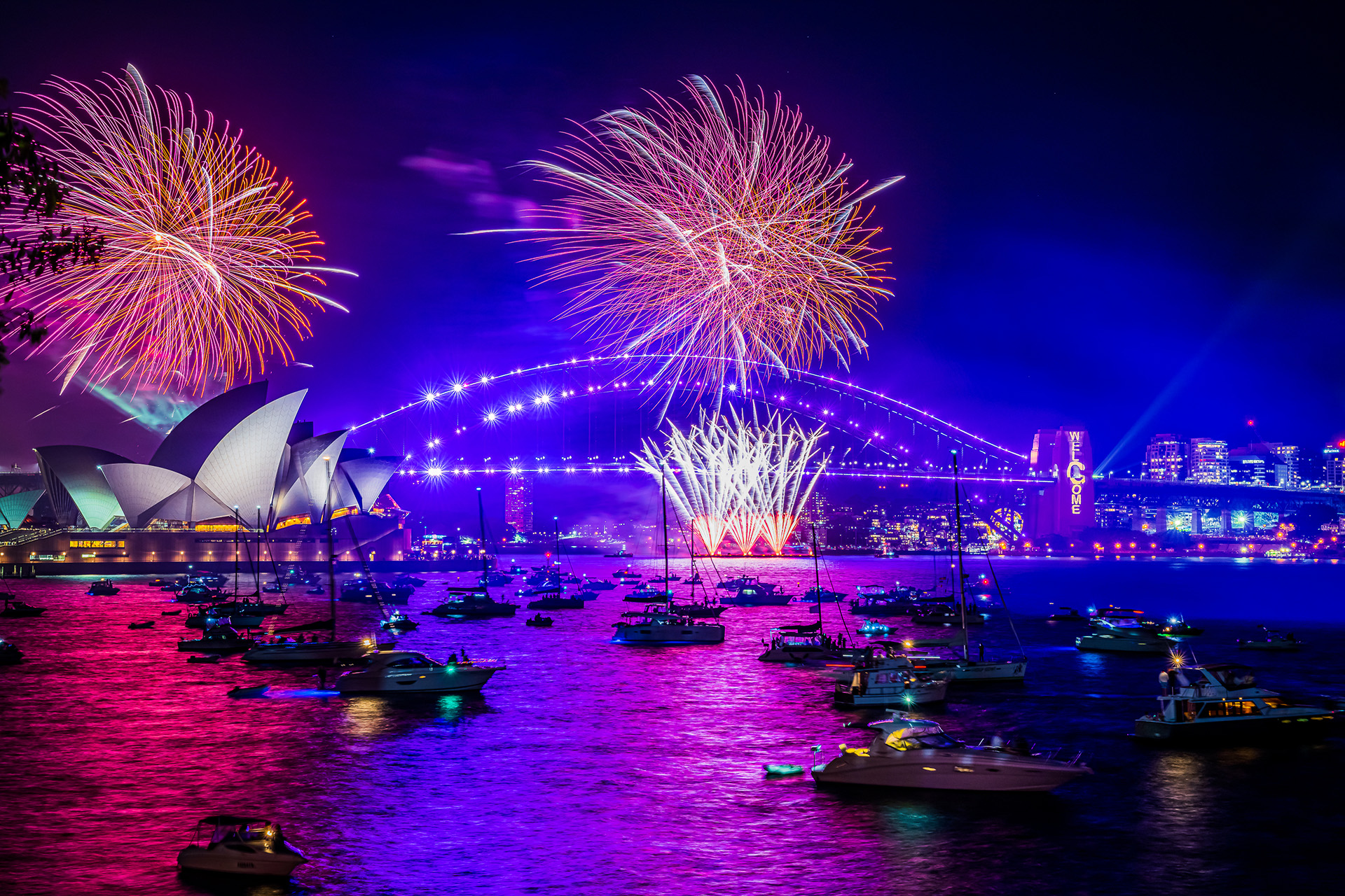 Wide shot of animated visuals projected onto the Sydney Harbour Bridge, flanked by fireworks, for New Years Eve 2021