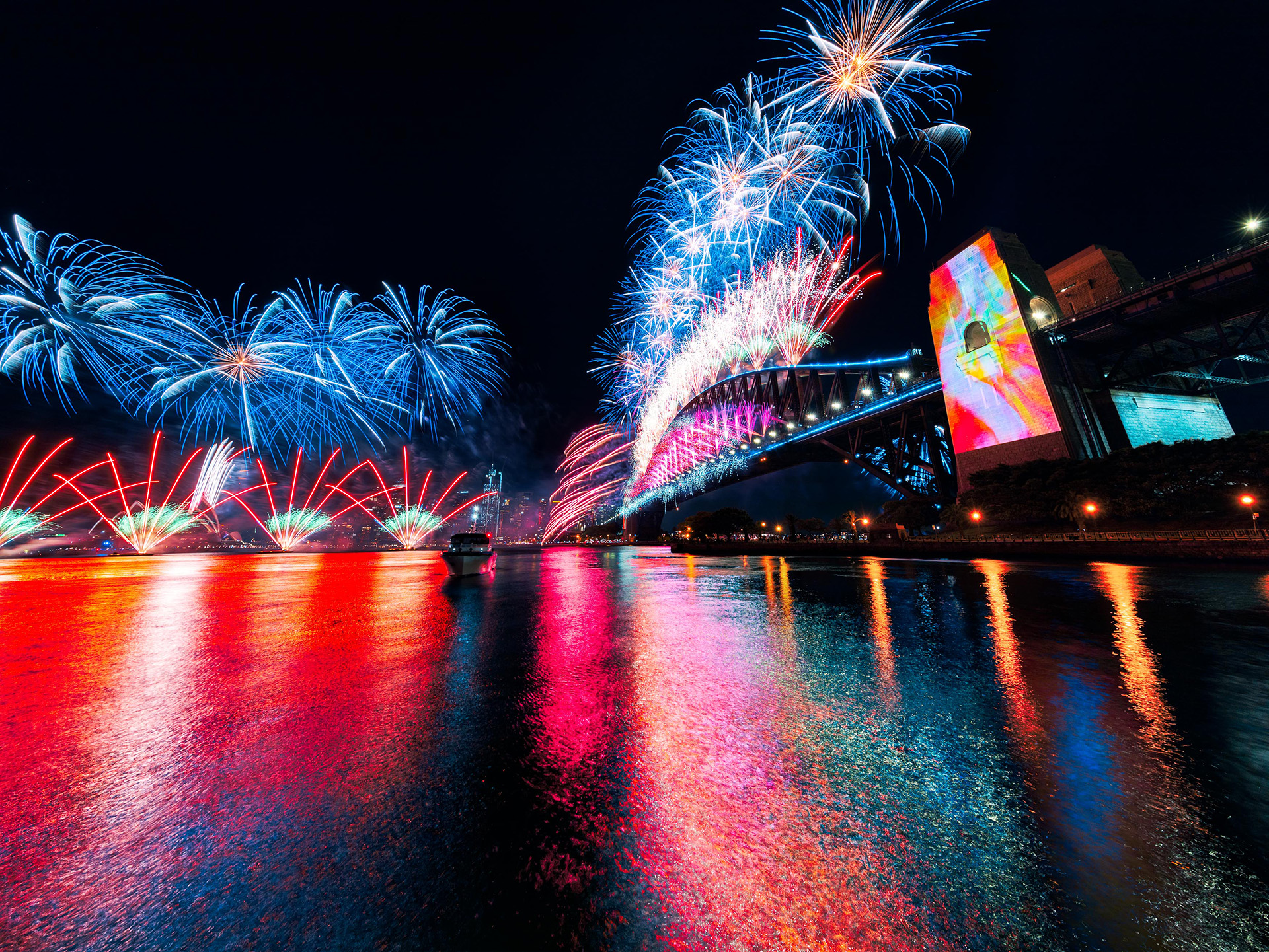Animated visuals projected onto the Sydney Harbour Bridge, flanked by fireworks, for New Years Eve 2021