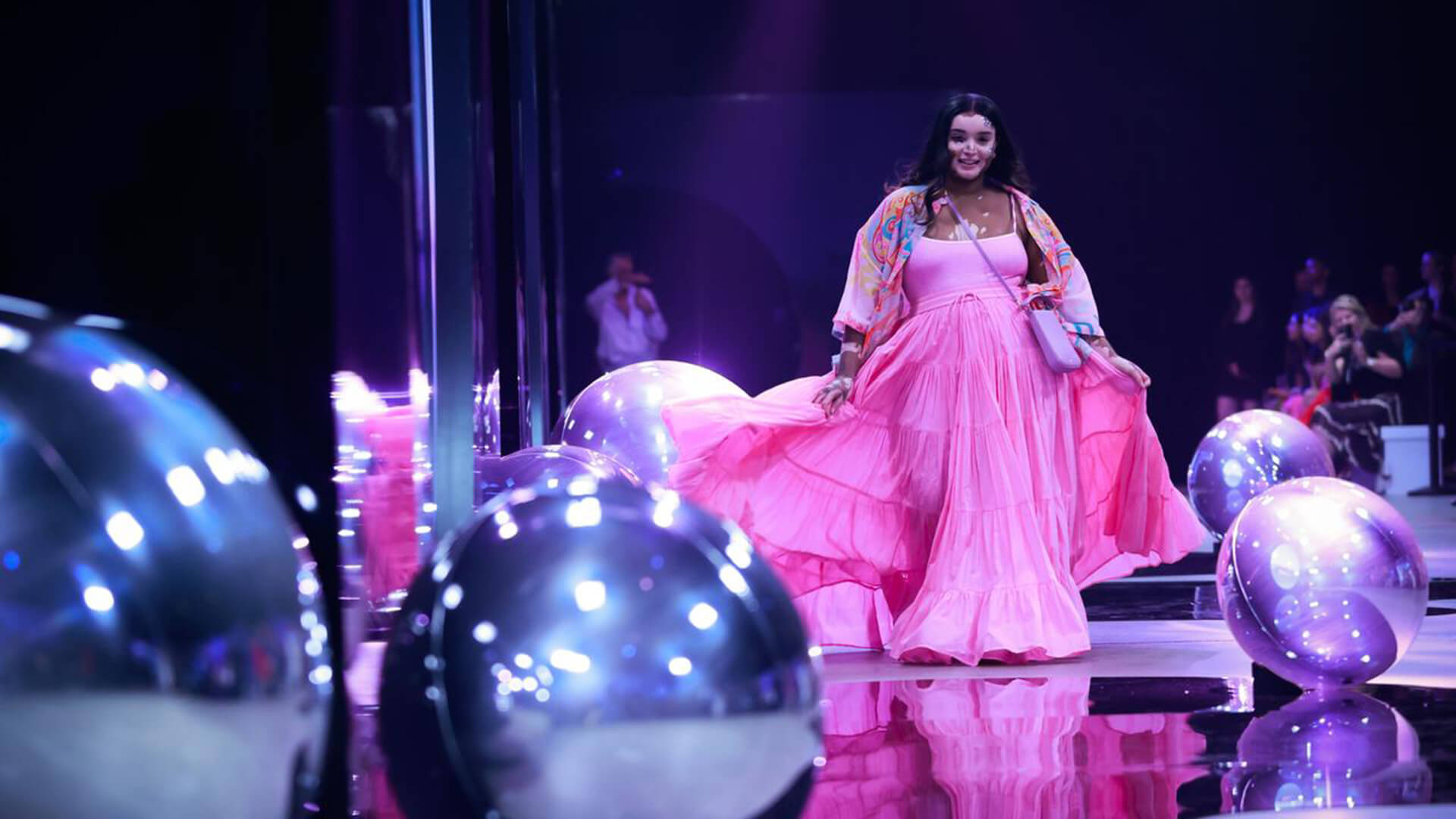 Woman in pink dress walking on fashion runway with silver reflective balls for The Iconic RUNWAY X fashion show.